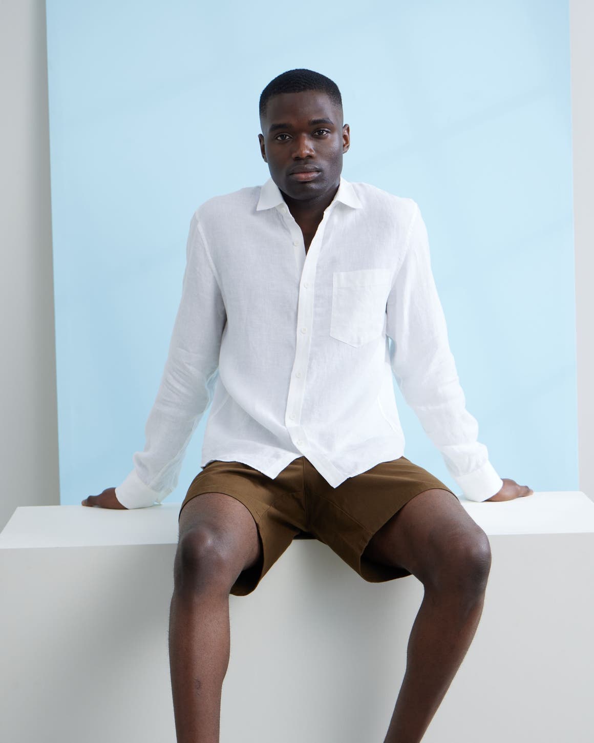 A man wearing a white button-up shirt and brown shorts.