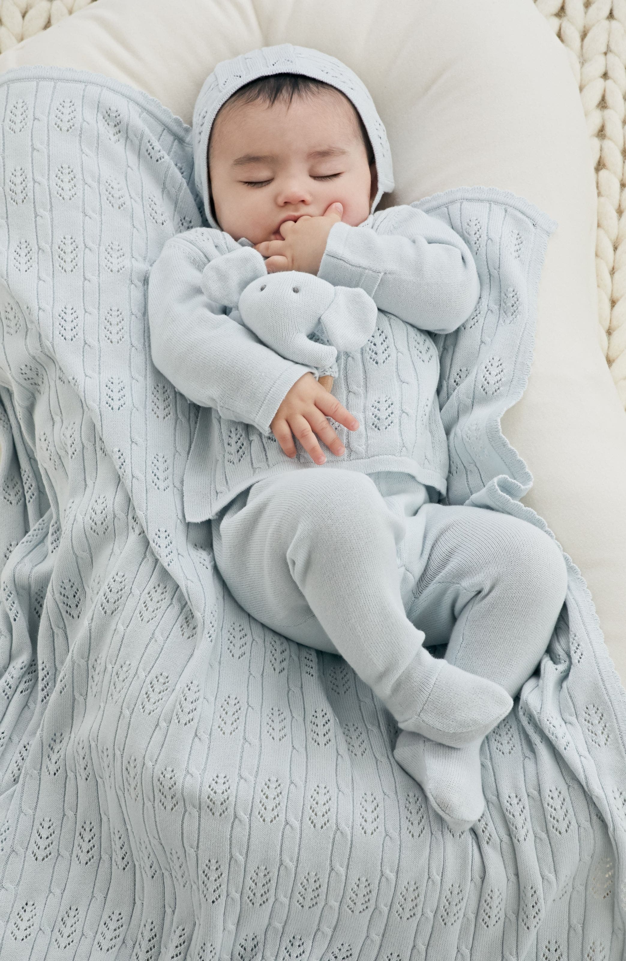  A baby wearing a pale-blue outfit and hat with a matching blanket and elephant stuffed animal.