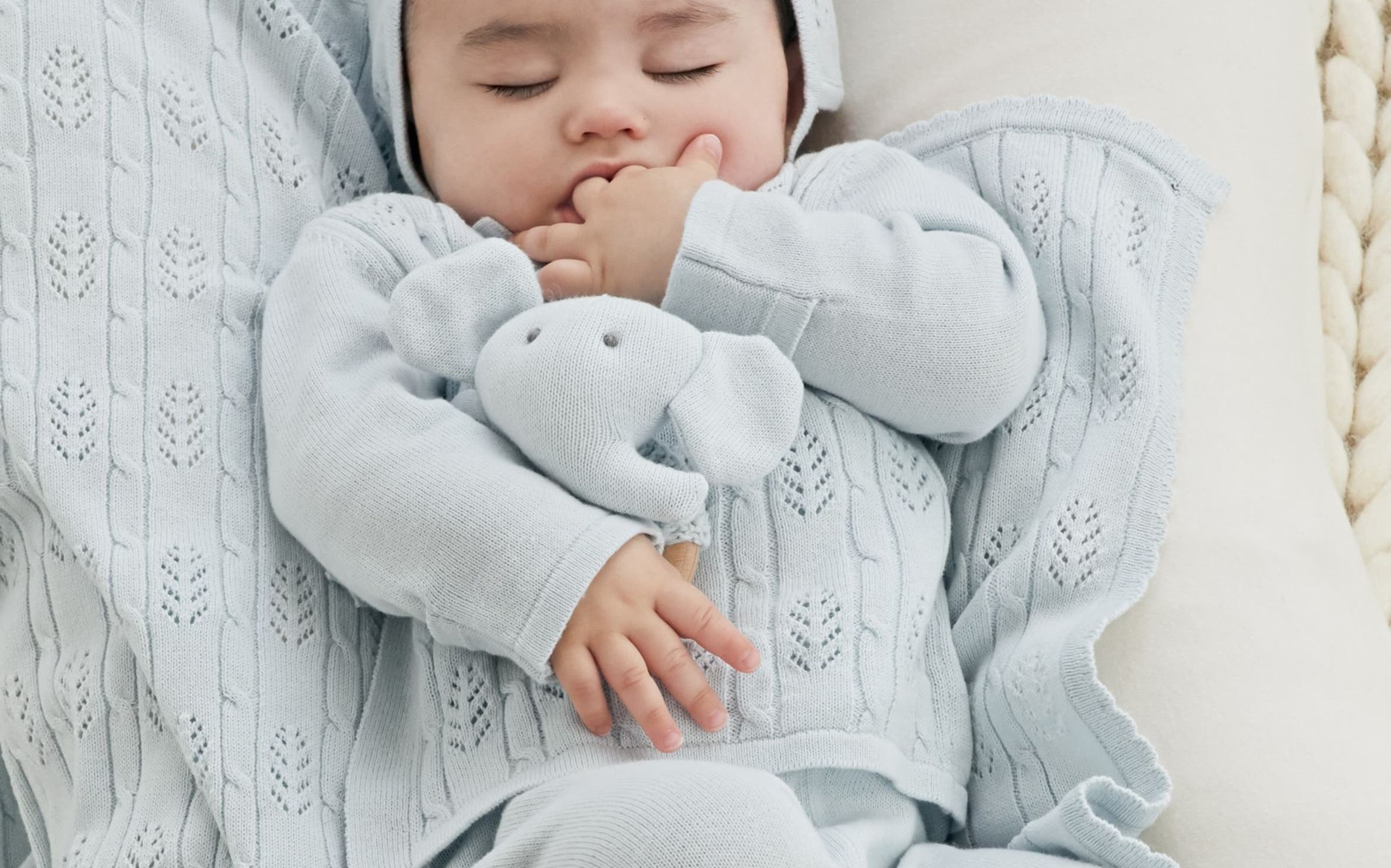 A baby wearing a pale-blue outfit and hat with a matching blanket and elephant stuffed animal.