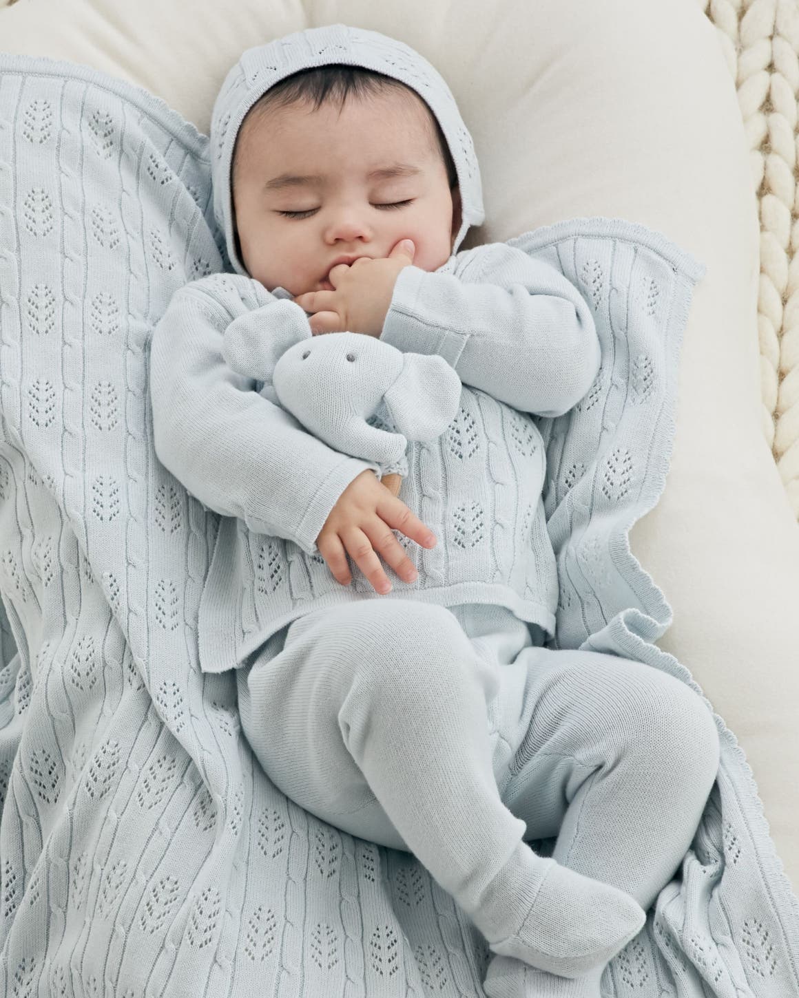 A baby wearing a pale-blue outfit and hat with a matching blanket and elephant stuffed animal.