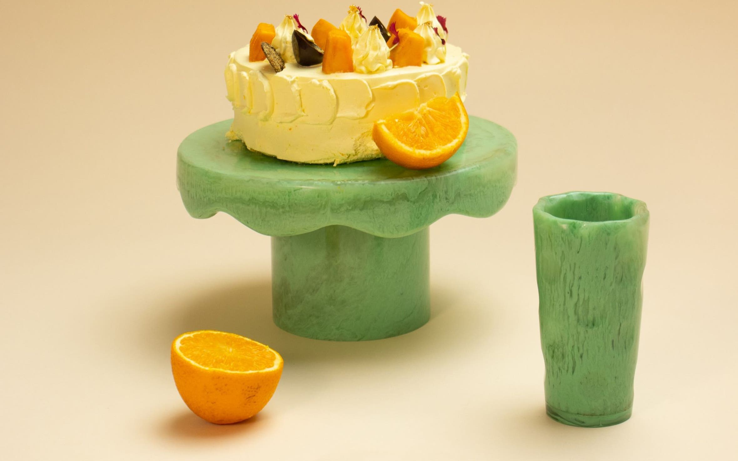 An orange cake on a green cake stand beside a matching cup.