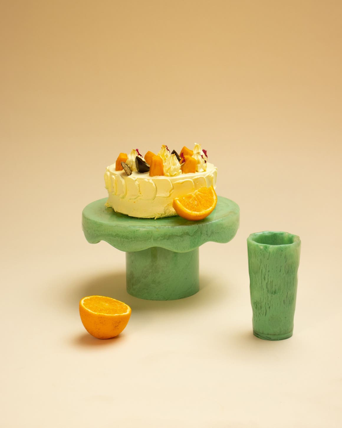 An orange cake on a green cake stand beside a matching cup.