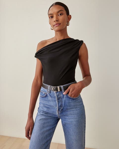 A woman wearing a black one-shoulder top with jeans.