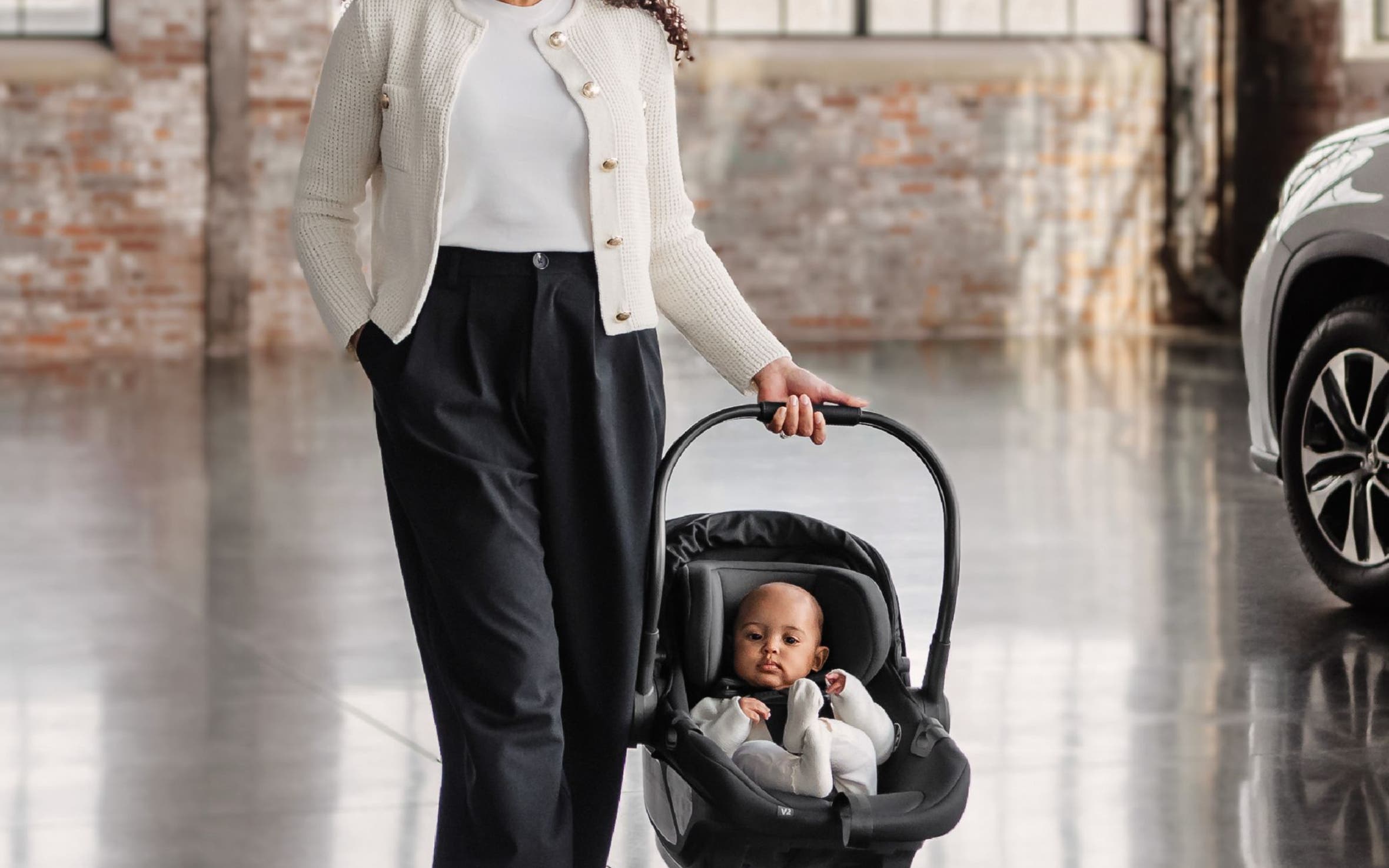 A woman carrying an infant in a baby car seat.