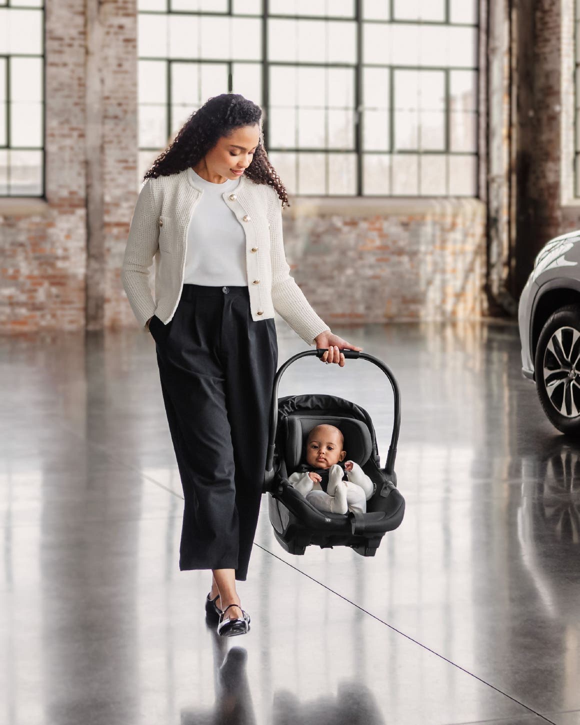 A woman carrying an infant in a baby car seat.