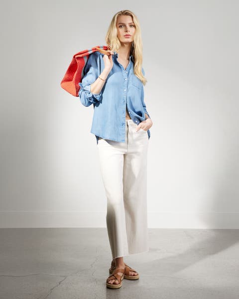 A woman wearing a chambray button up top and white pants. 