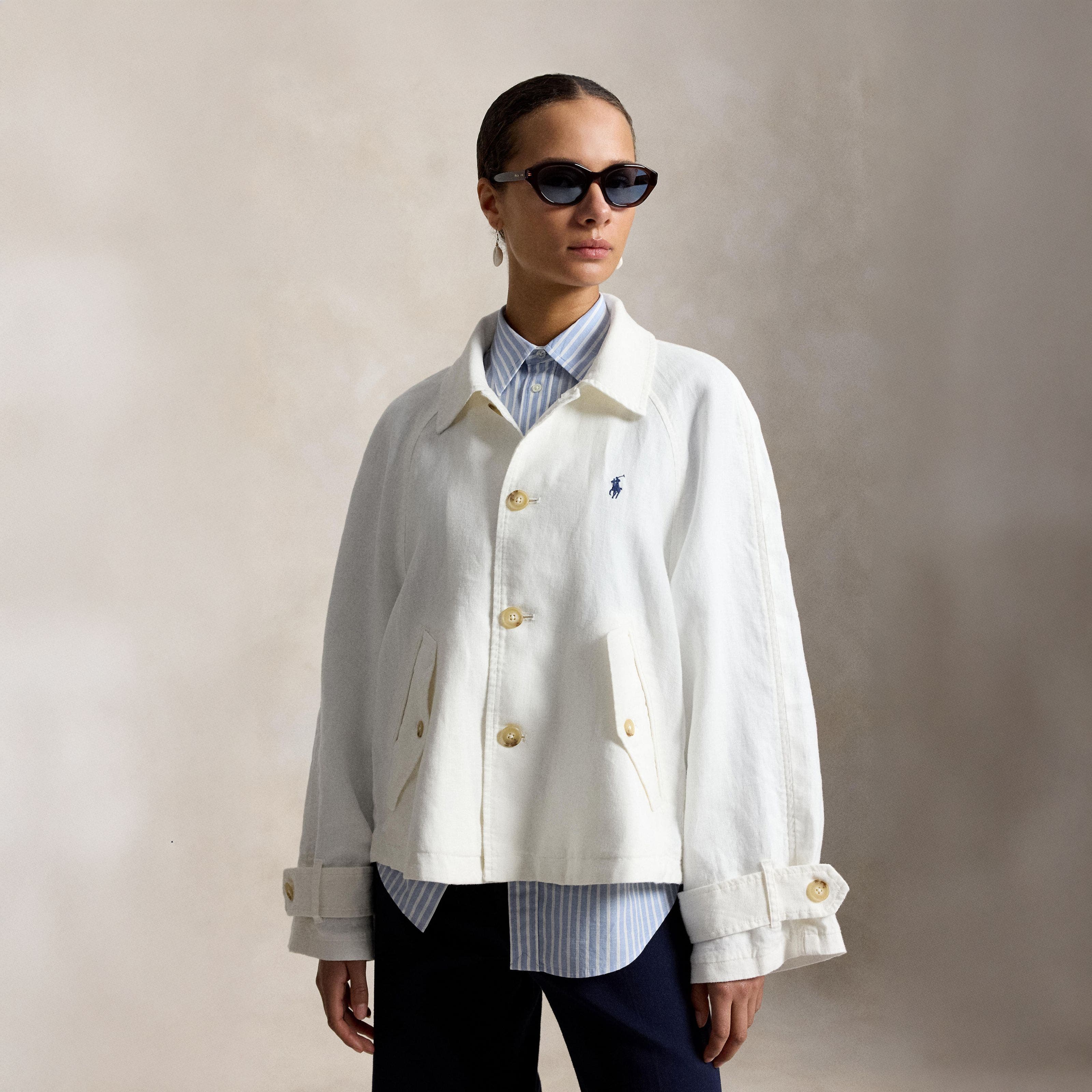 A woman in a white Ralph Lauren Polo canvas jacket, layered over a blue striped shirt and dark wide-legged pants.