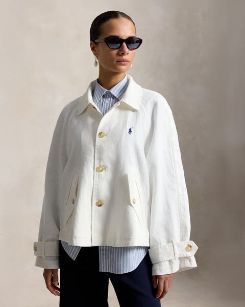 A woman in a white Ralph Lauren Polo canvas jacket, layered over a blue striped shirt and dark wide-legged pants.