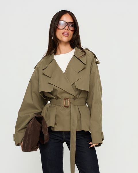 A woman in a cropped army green trench coat over dark-rinse jeans.