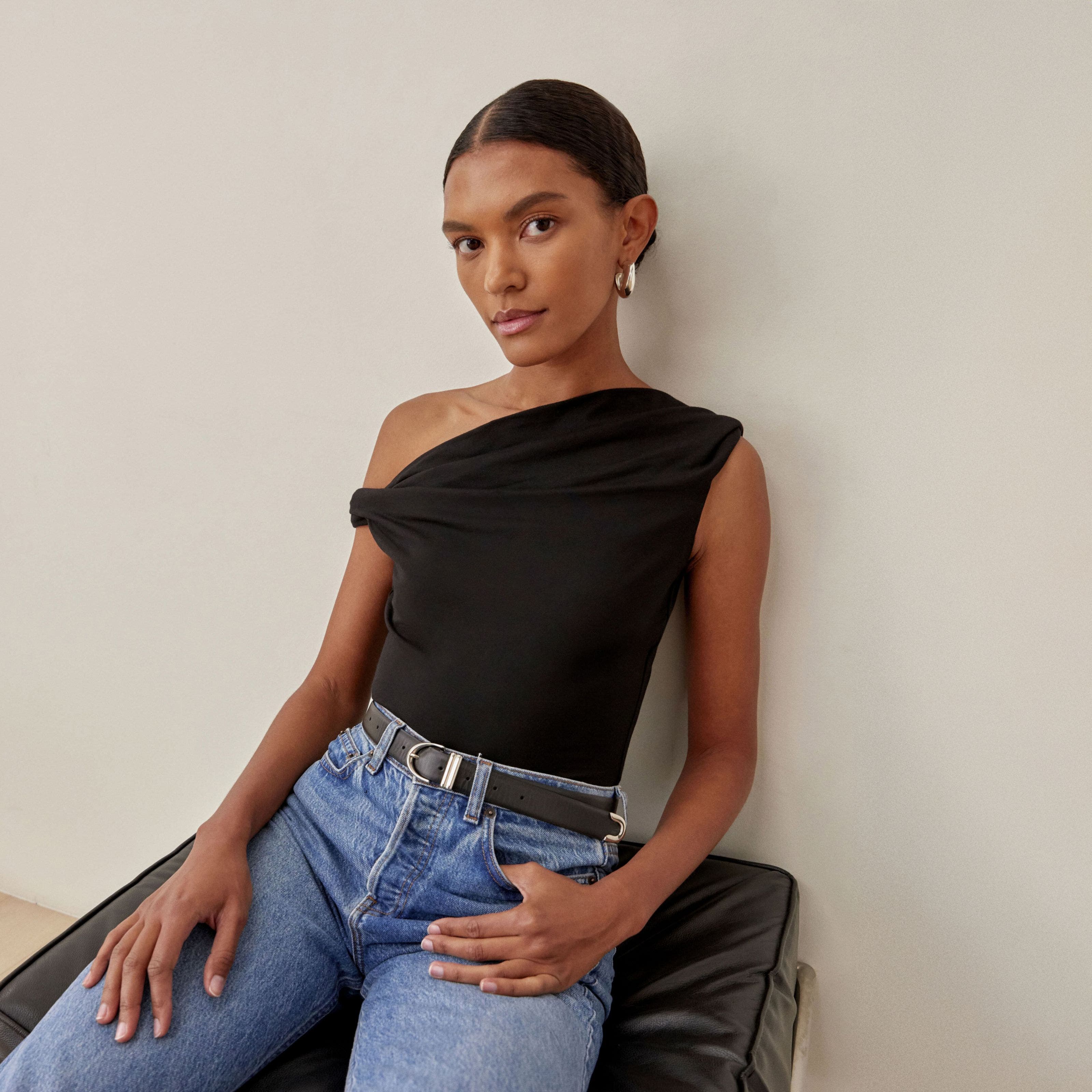A woman wearing a black off-the-shoulder top and a pair of jeans.