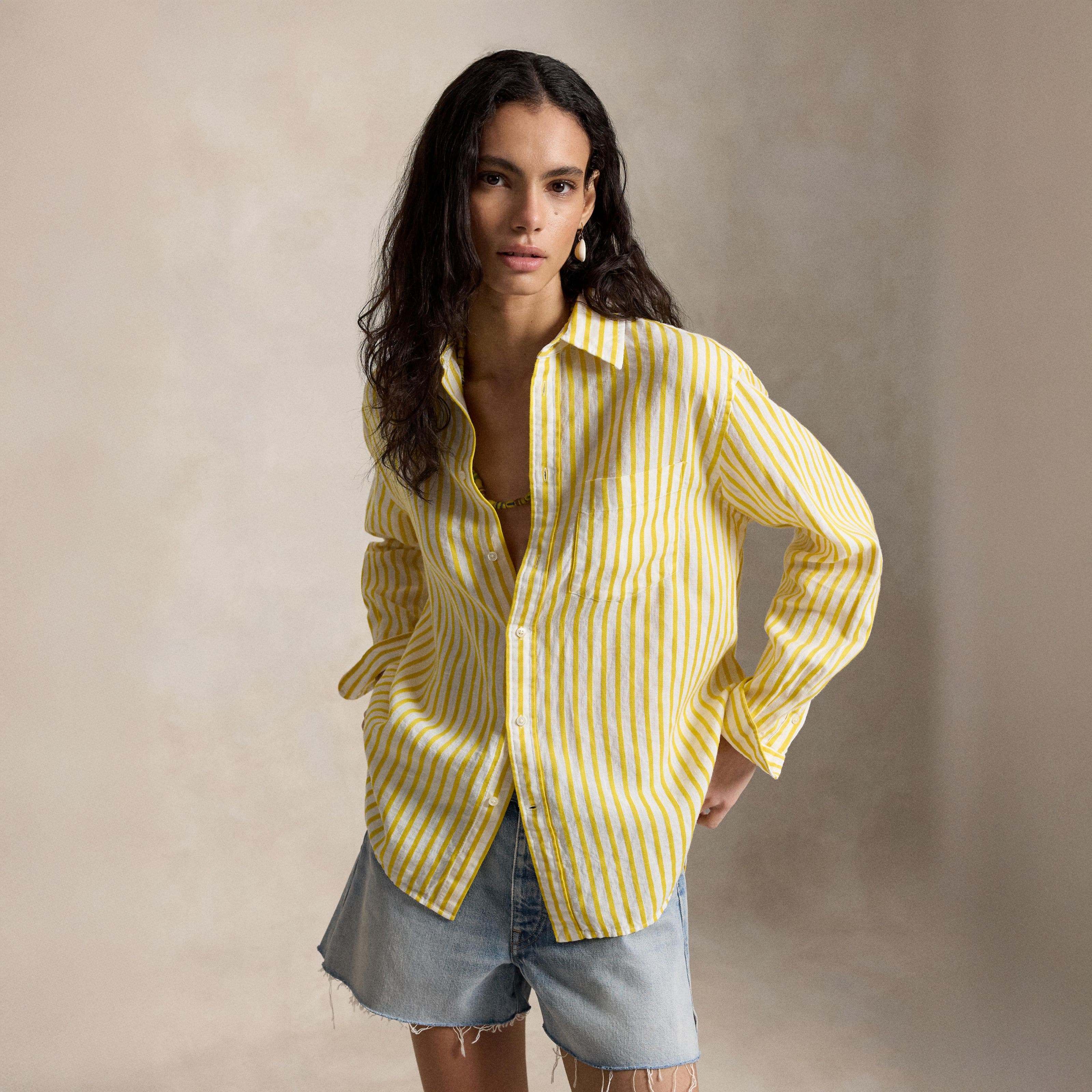 A woman wearing a yellow striped polo and denim shorts.