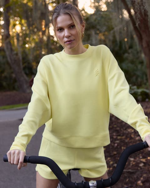 A woman wearing a matching yellow active sweatshirt and shorts.
