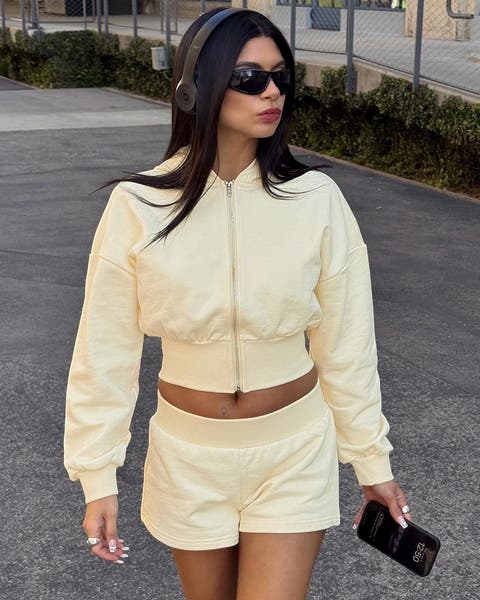 A woman wearing a cropped, yellow sweatshirt and matching shorts.
