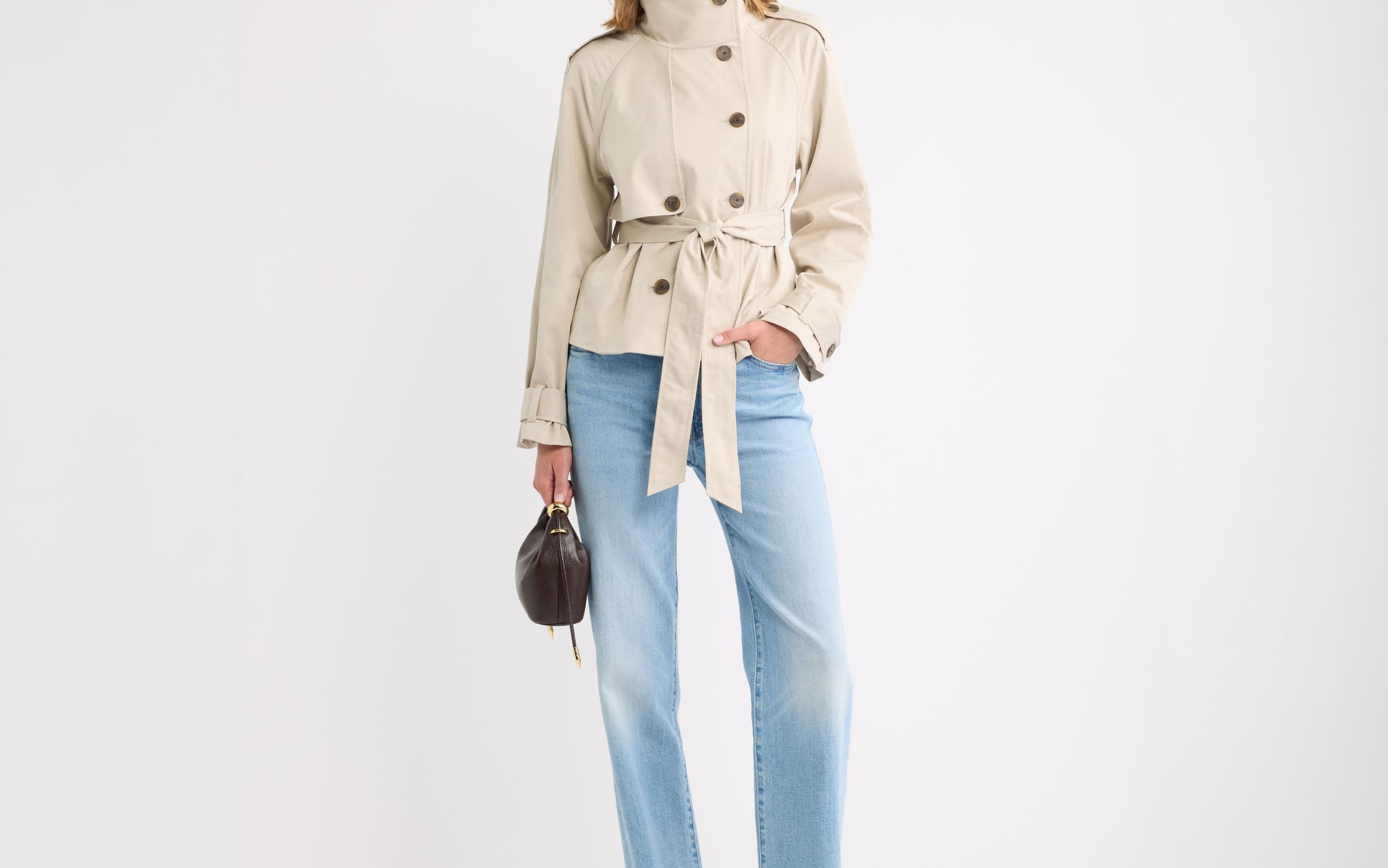 A woman in a cropped tan trench coat and light wash jeans.