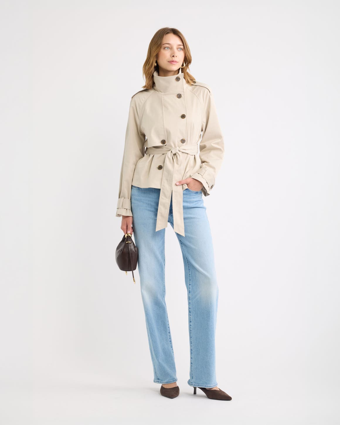 A woman in a cropped tan trench coat and light wash jeans.