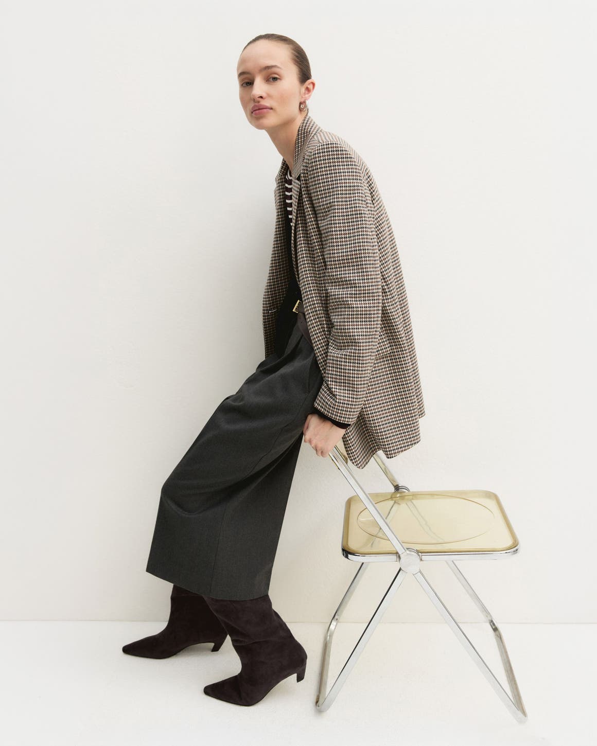 A woman in a plaid blazer and black midi skirt with boots.