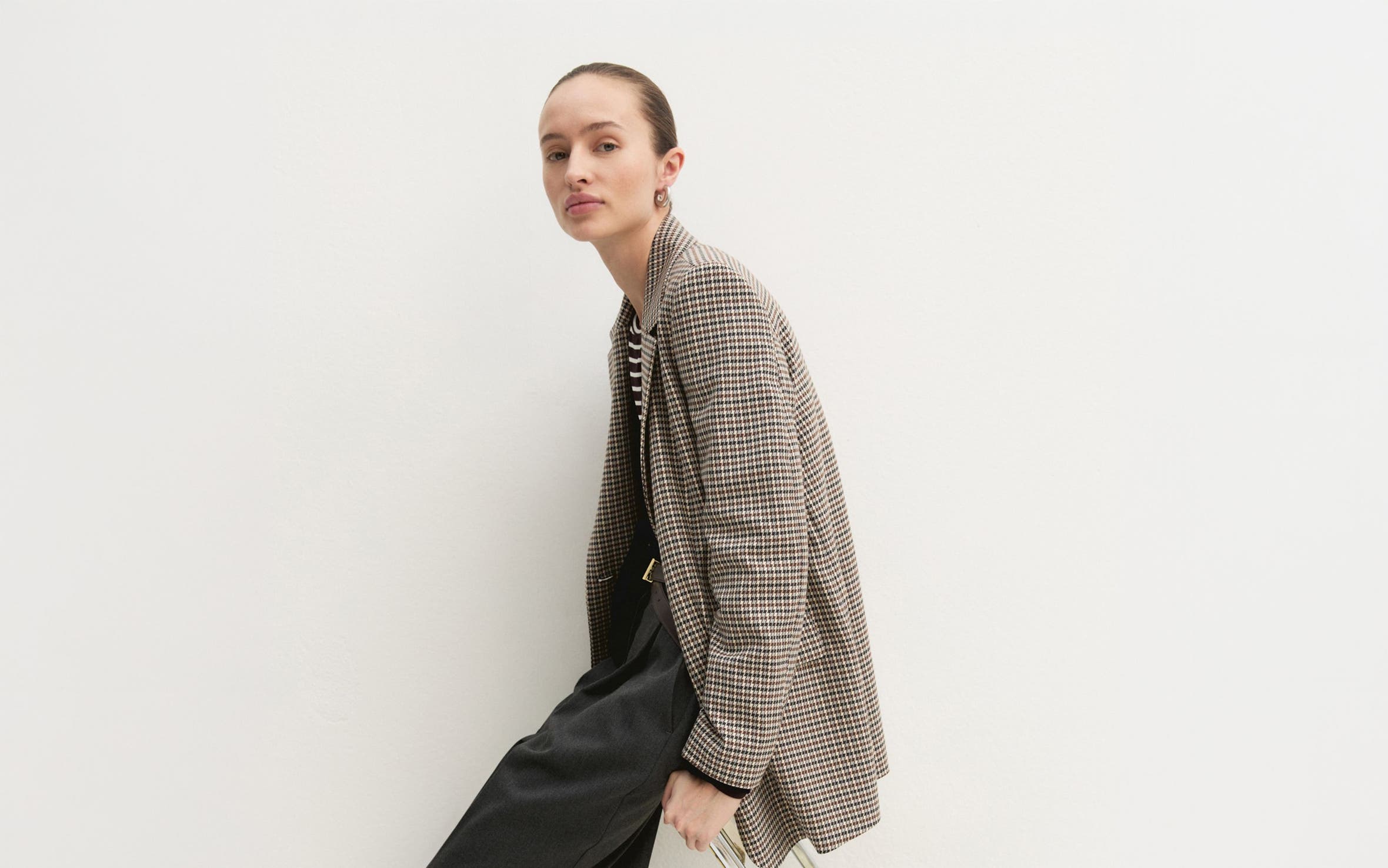 A woman in a plaid blazer and black midi skirt with boots.