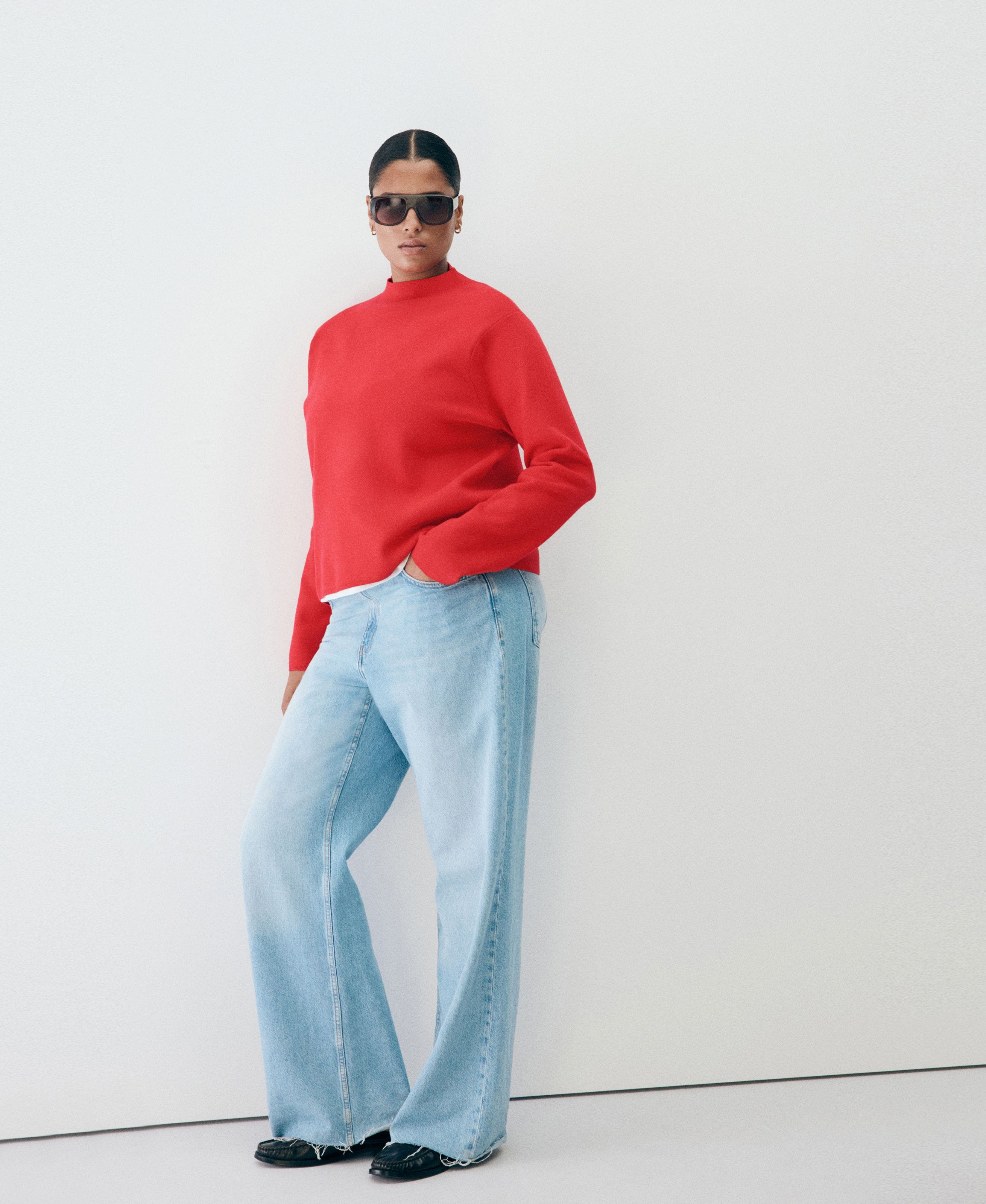 A woman in a red mock-neck sweater, light wash jeans.