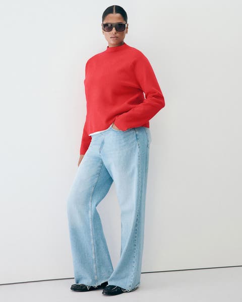 A woman in a red mock-neck sweater, light wash jeans.