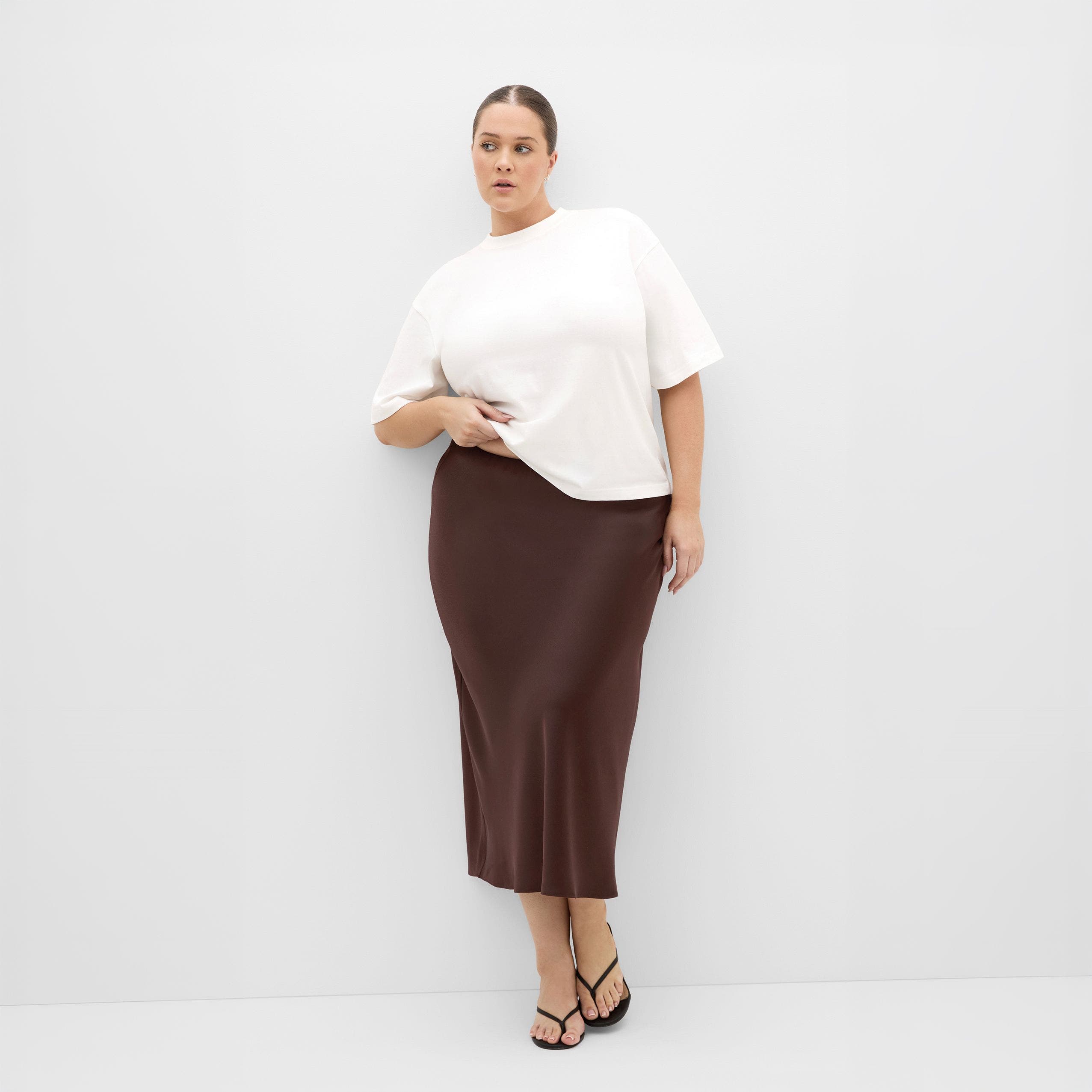 A woman in a white top and brown satin midi skirt.