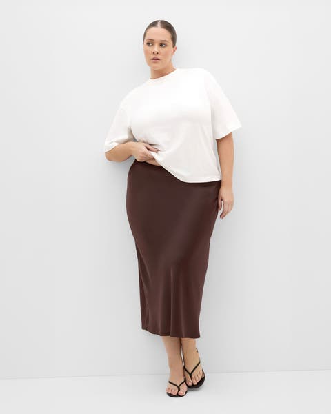 A woman in a white top and brown satin midi skirt.