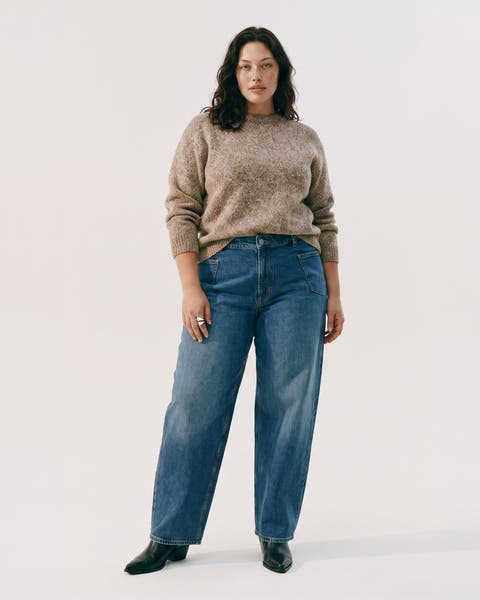 A woman in a beige knit sweater and barrel leg jeans.