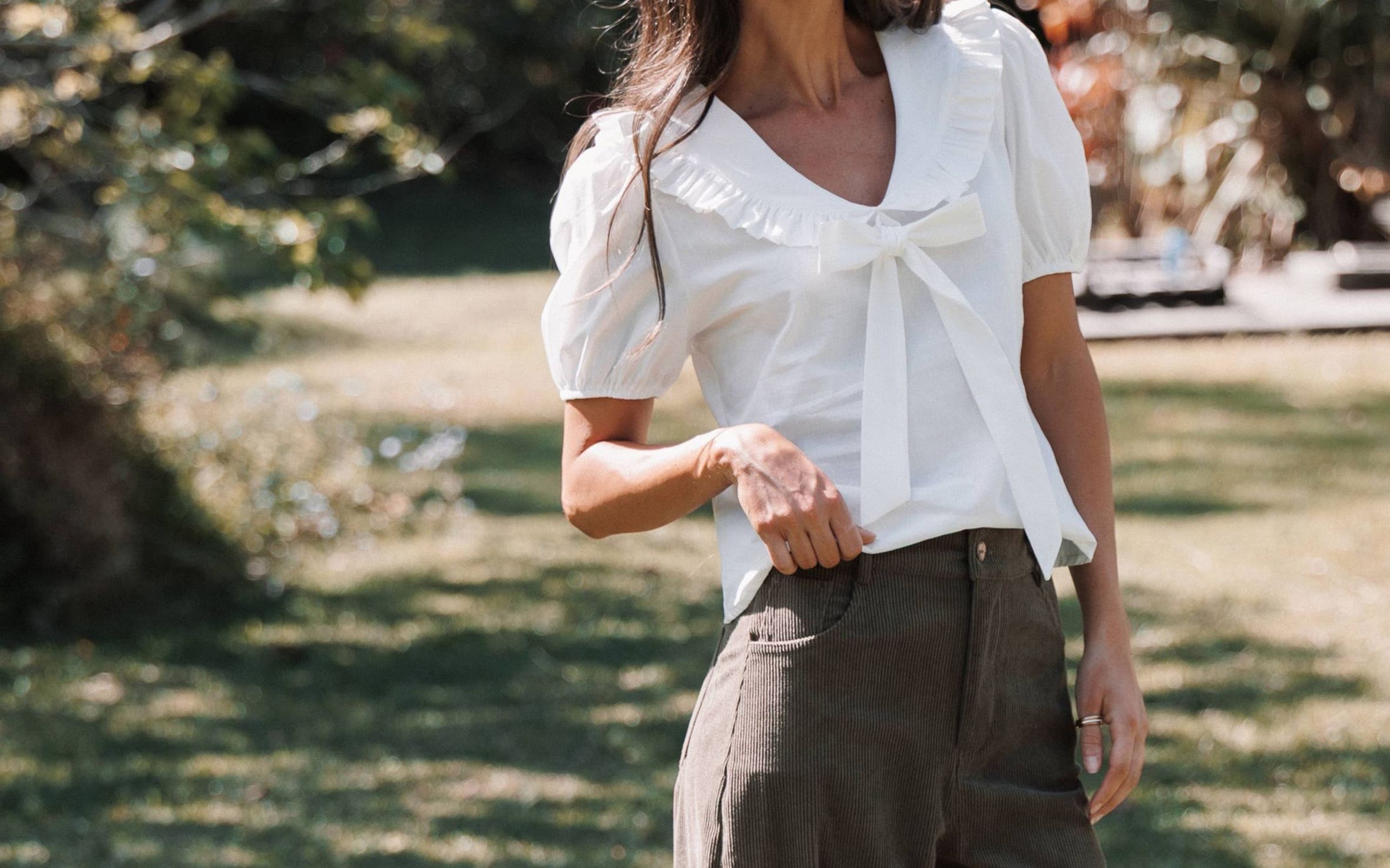 A woman in a white blouse and brown corduroy pants.