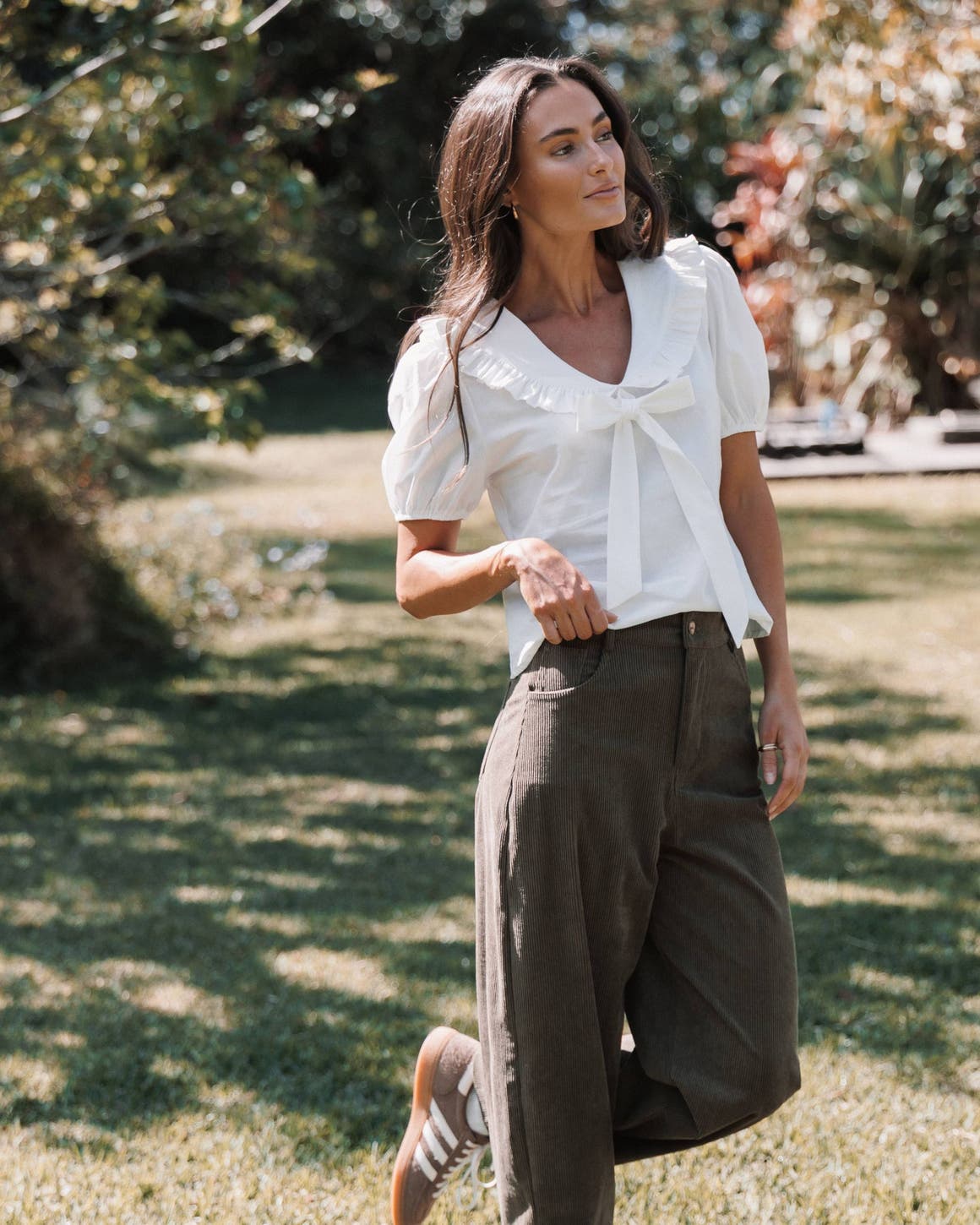 A woman in a white blouse and brown corduroy pants.