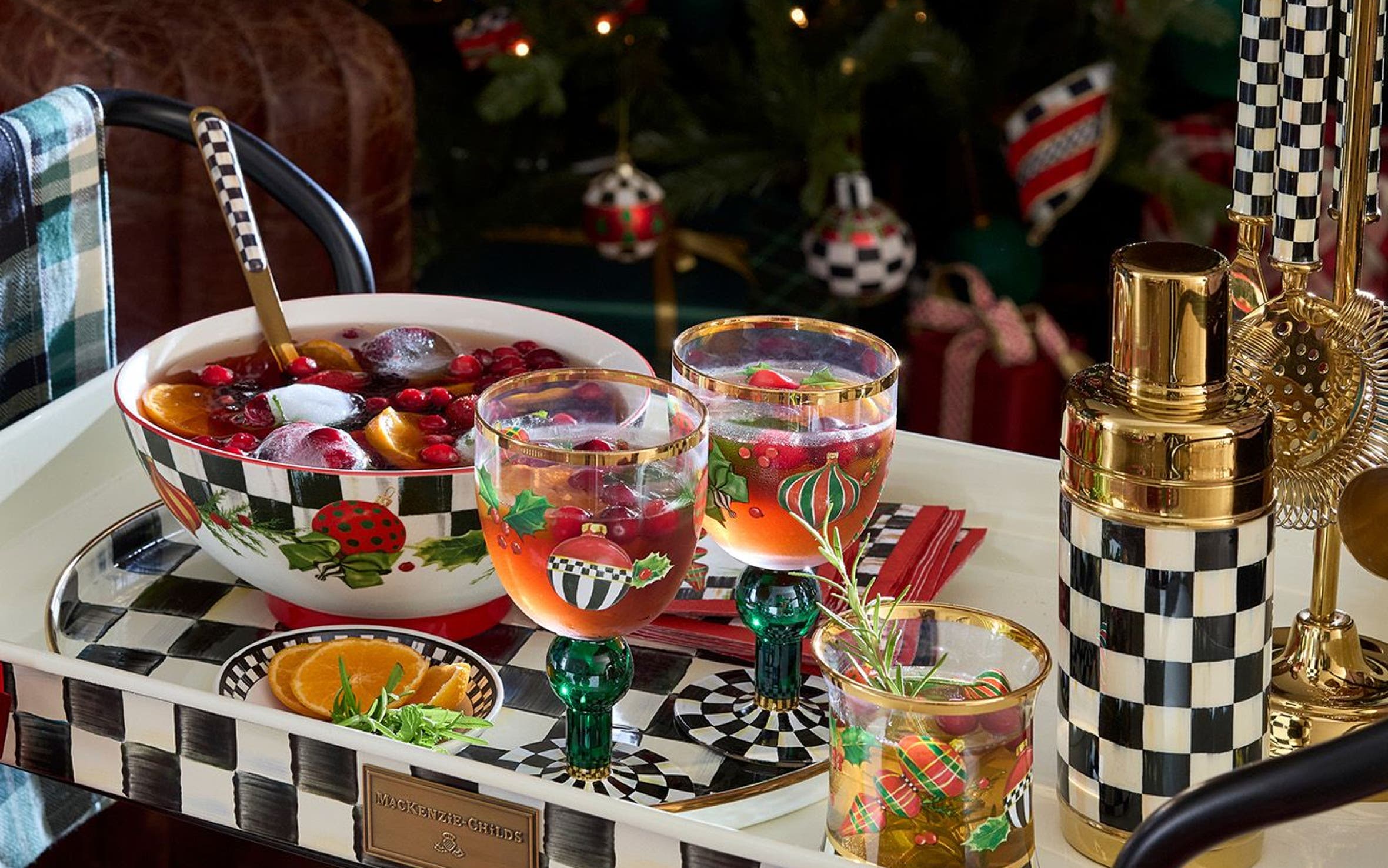 Mackenzie-Childs holiday bar cart styled with a decorative punch bowl, glassware and wine cooler by a Christmas tree.