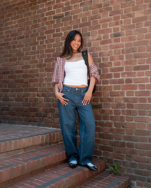 A woman wearing a tank top, plaid shirt, jeans, flats and backpack.