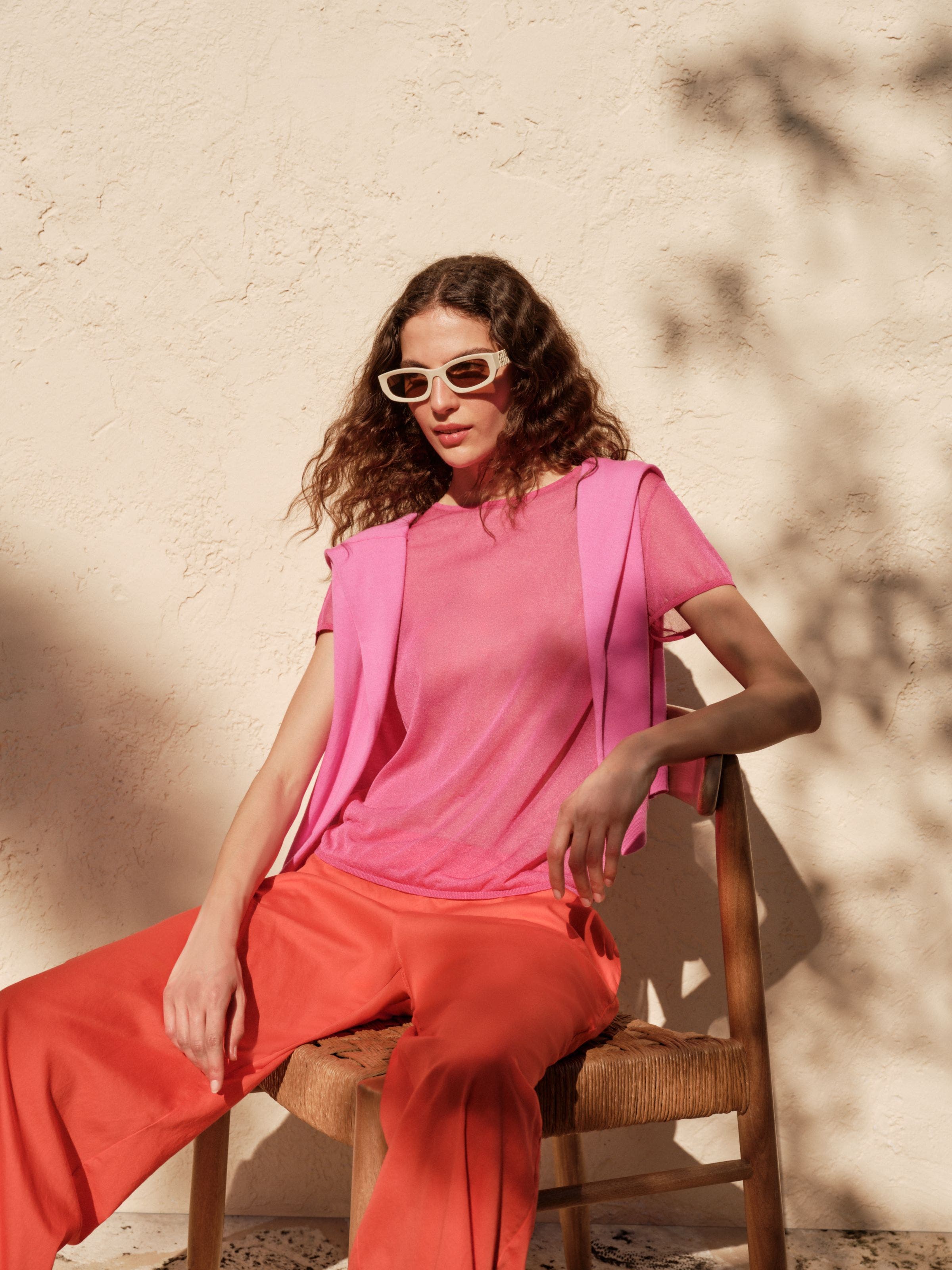 A woman wearing red linen pants and a pink t-shirt and sweater.