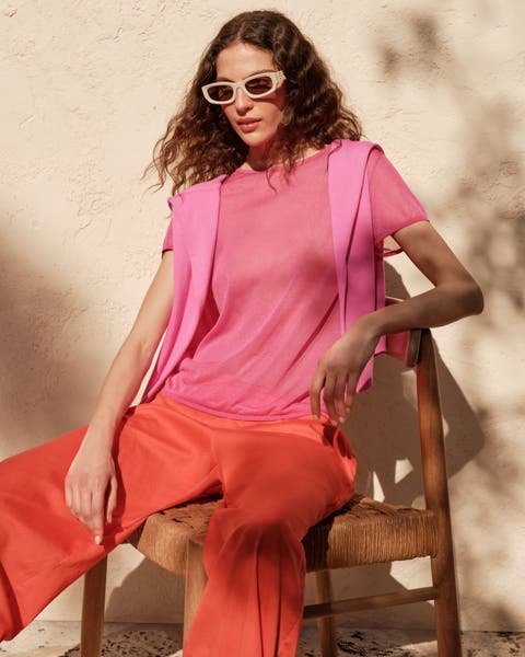 A woman wearing red linen pants and a pink t-shirt and sweater.