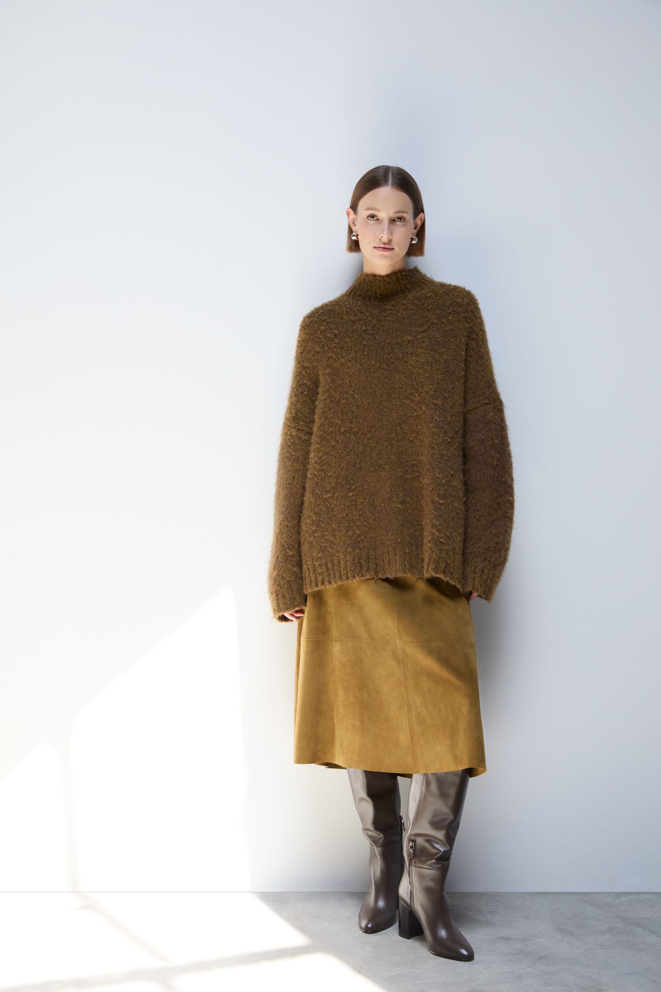 A woman wearing a brown sweater and skirt.