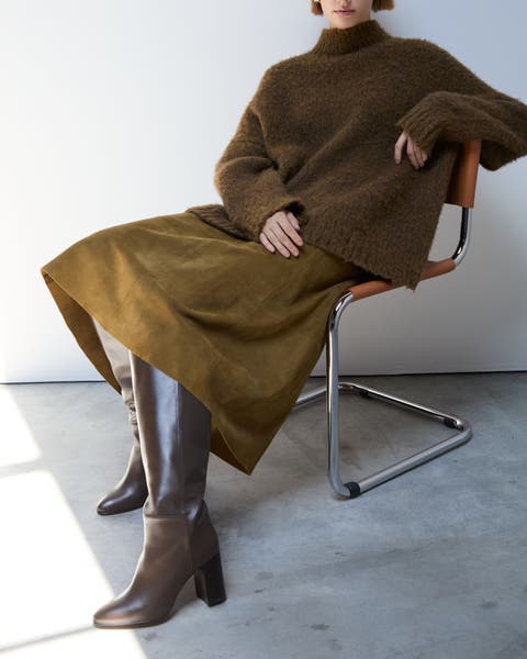 A woman wearing brown leather knee-high boots, an olive green midi skirt and oversized sweater.
