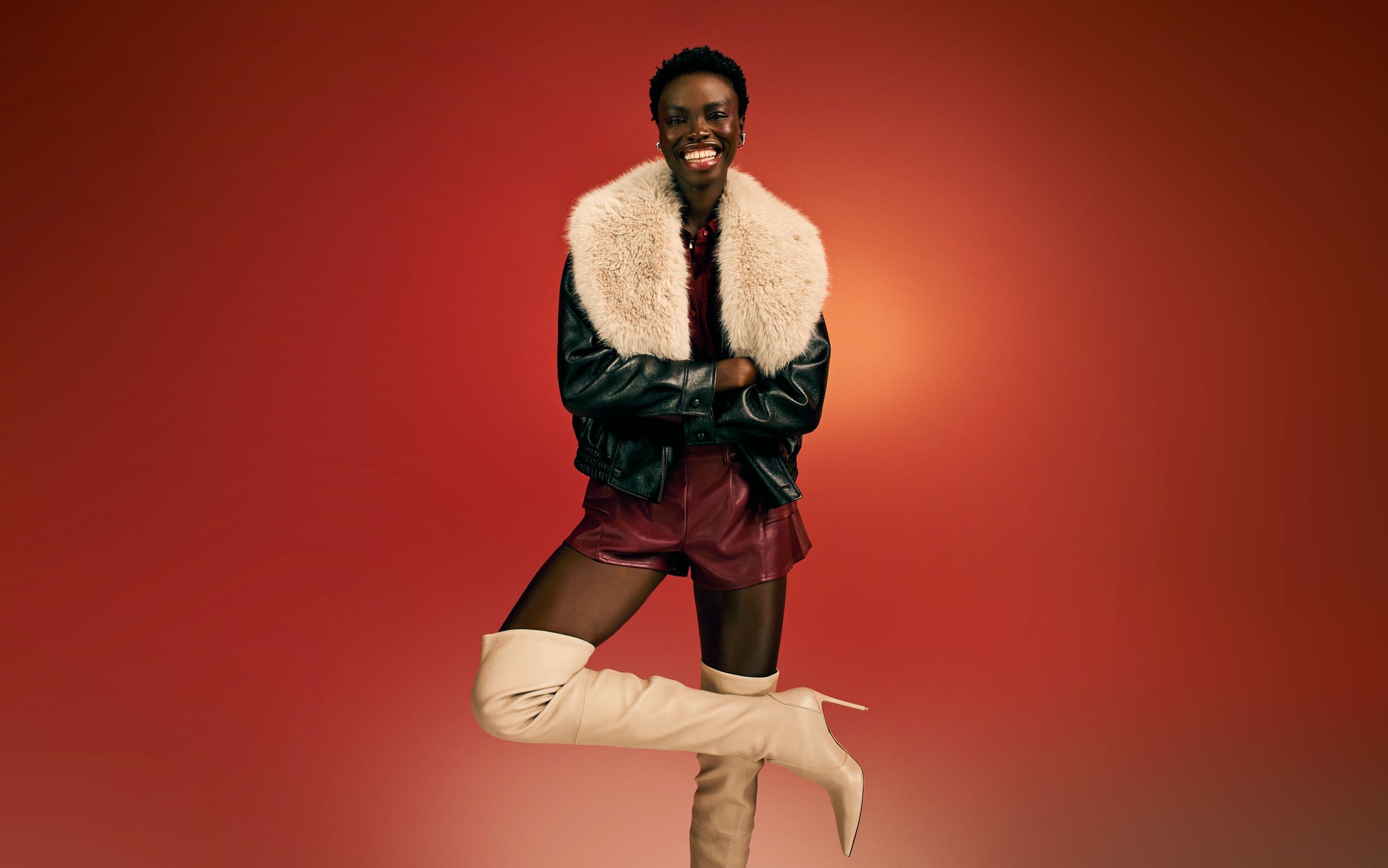 A woman wearing thigh-high boots, a burgundy skirt and a black jacket with a faux-fur collar.