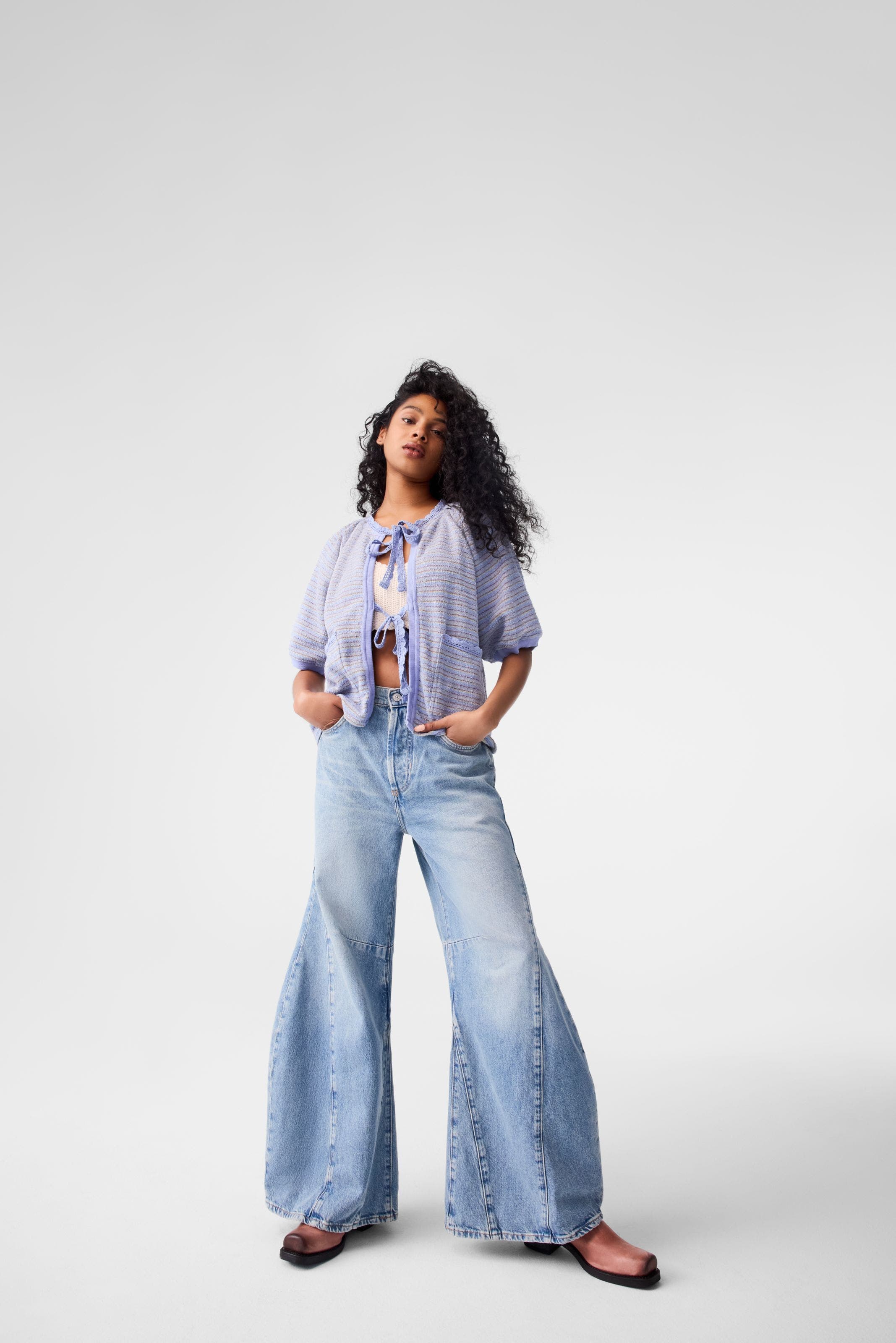 A woman wearing barrel jeans with a lavender cardigan and brown boots. 