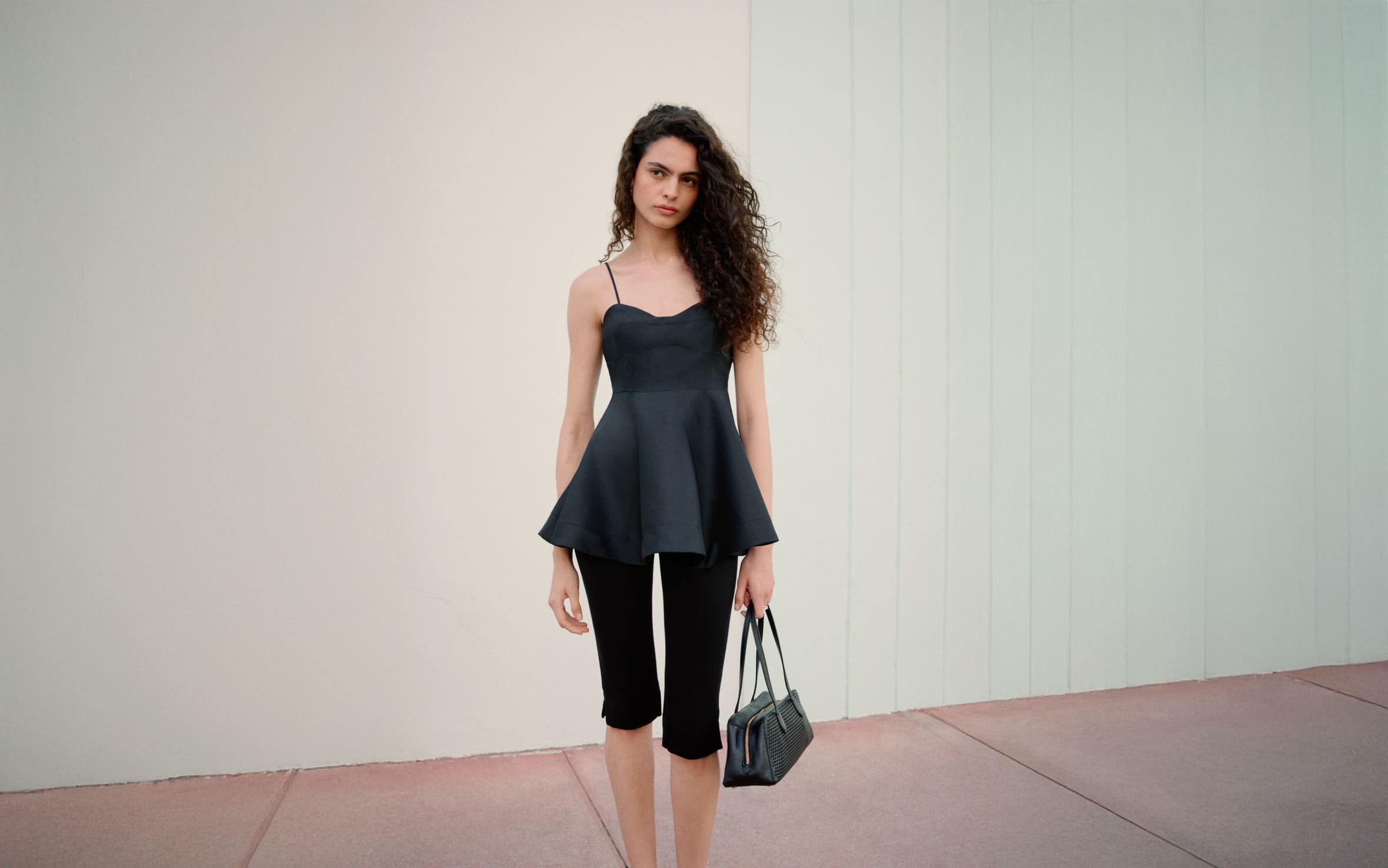 Woman wearing a black peplum top, capri pants and handbag.