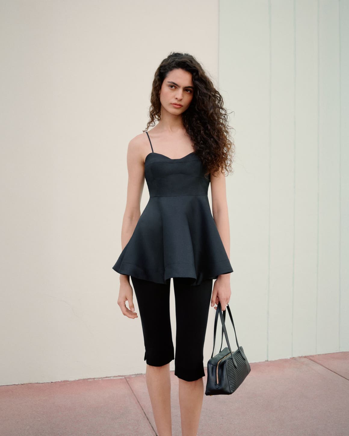 Woman wearing a black peplum top, capri pants and handbag.