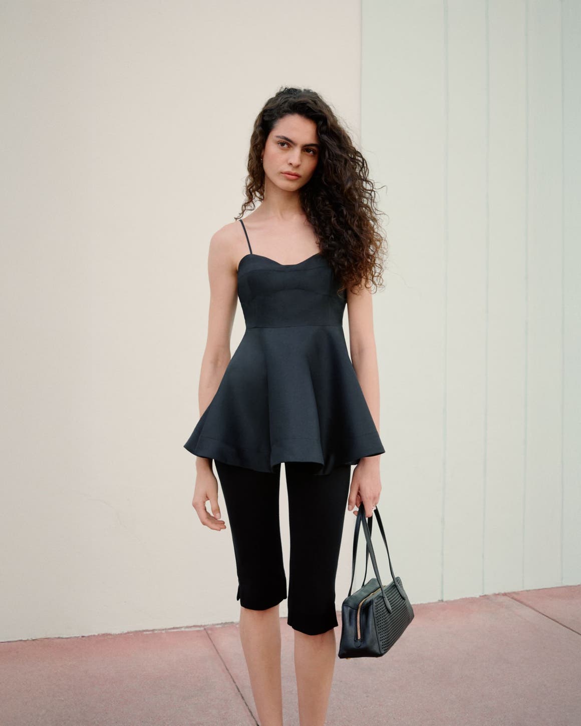 Woman wearing a black peplum top, capri pants and handbag.