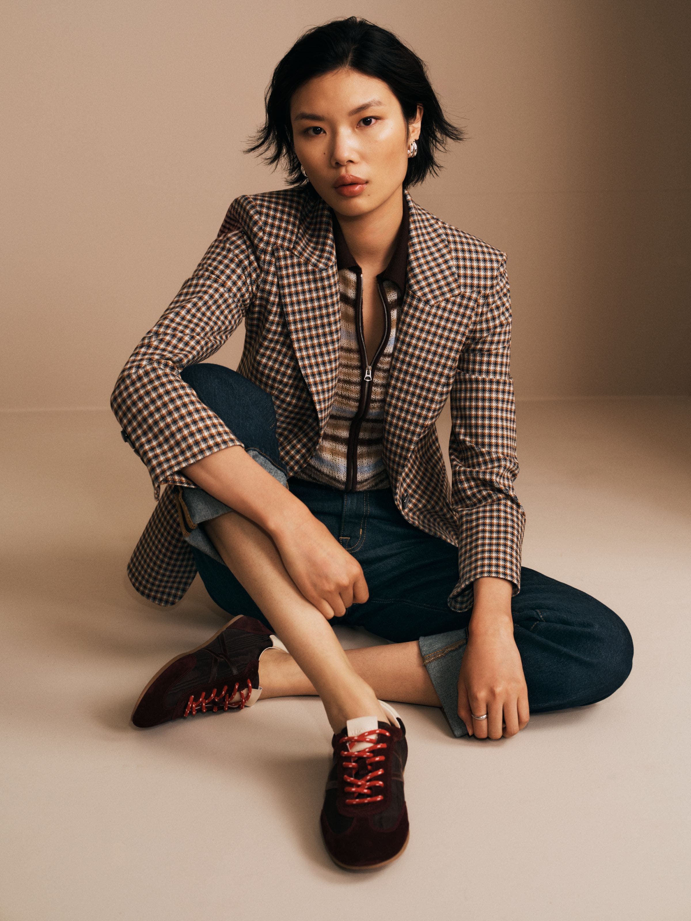 A woman wearing a blazer, jeans and brown sneakers.