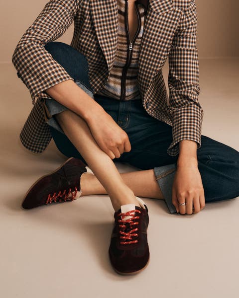 A woman wearing a blazer, jeans and brown sneakers.