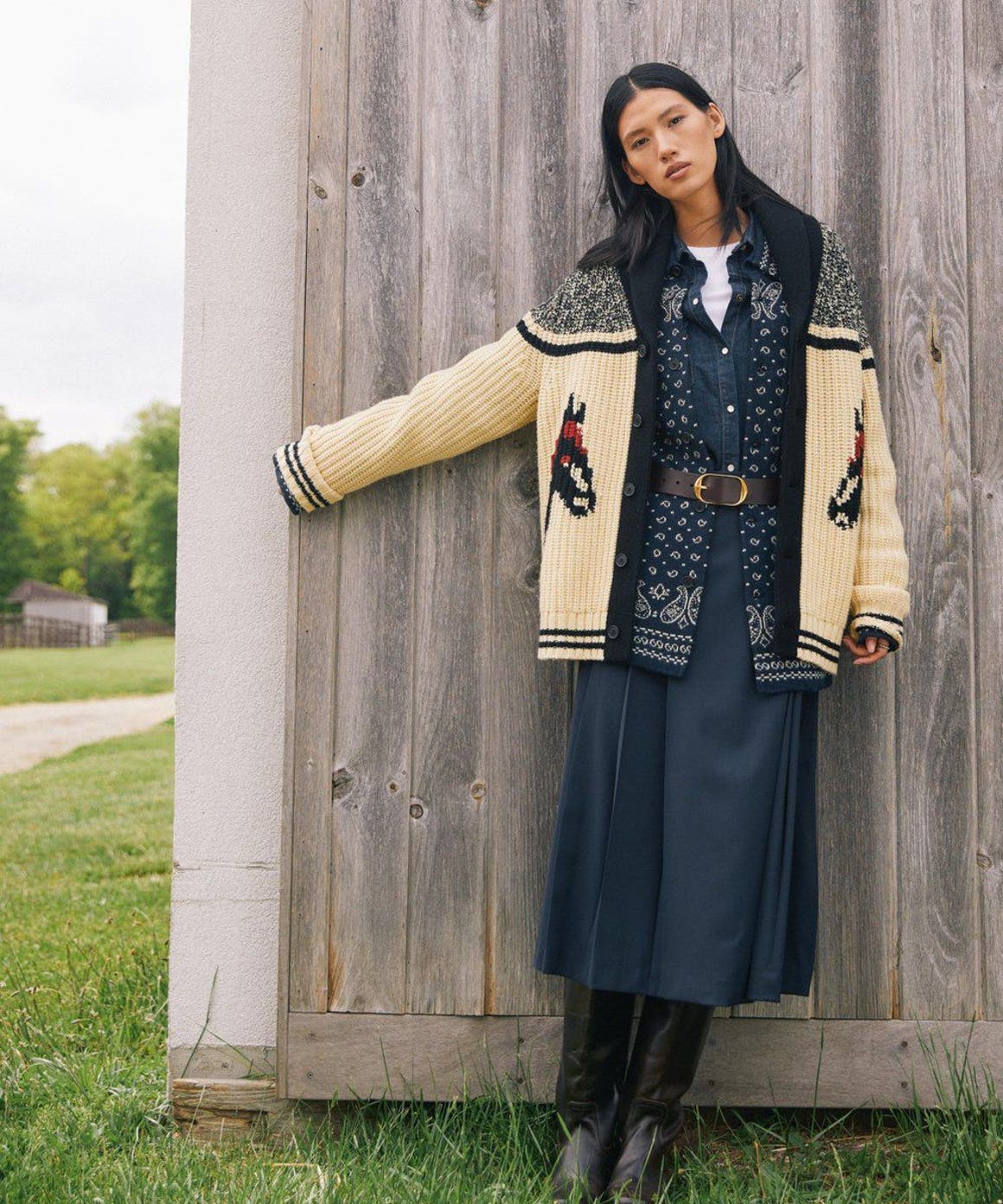 A woman wearing layered boho outfit by wooden wall.