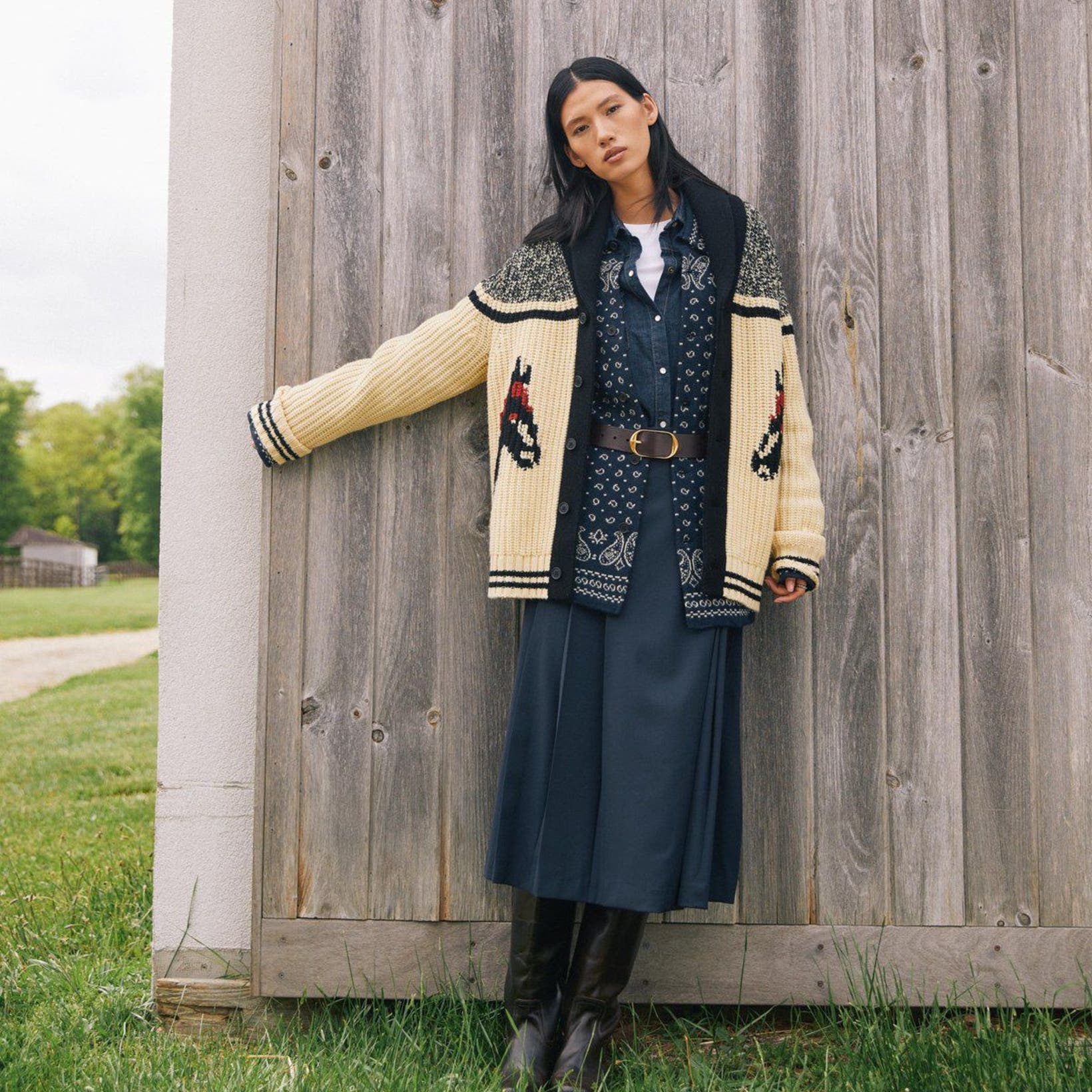 A woman wearing layered boho outfit by wooden wall.