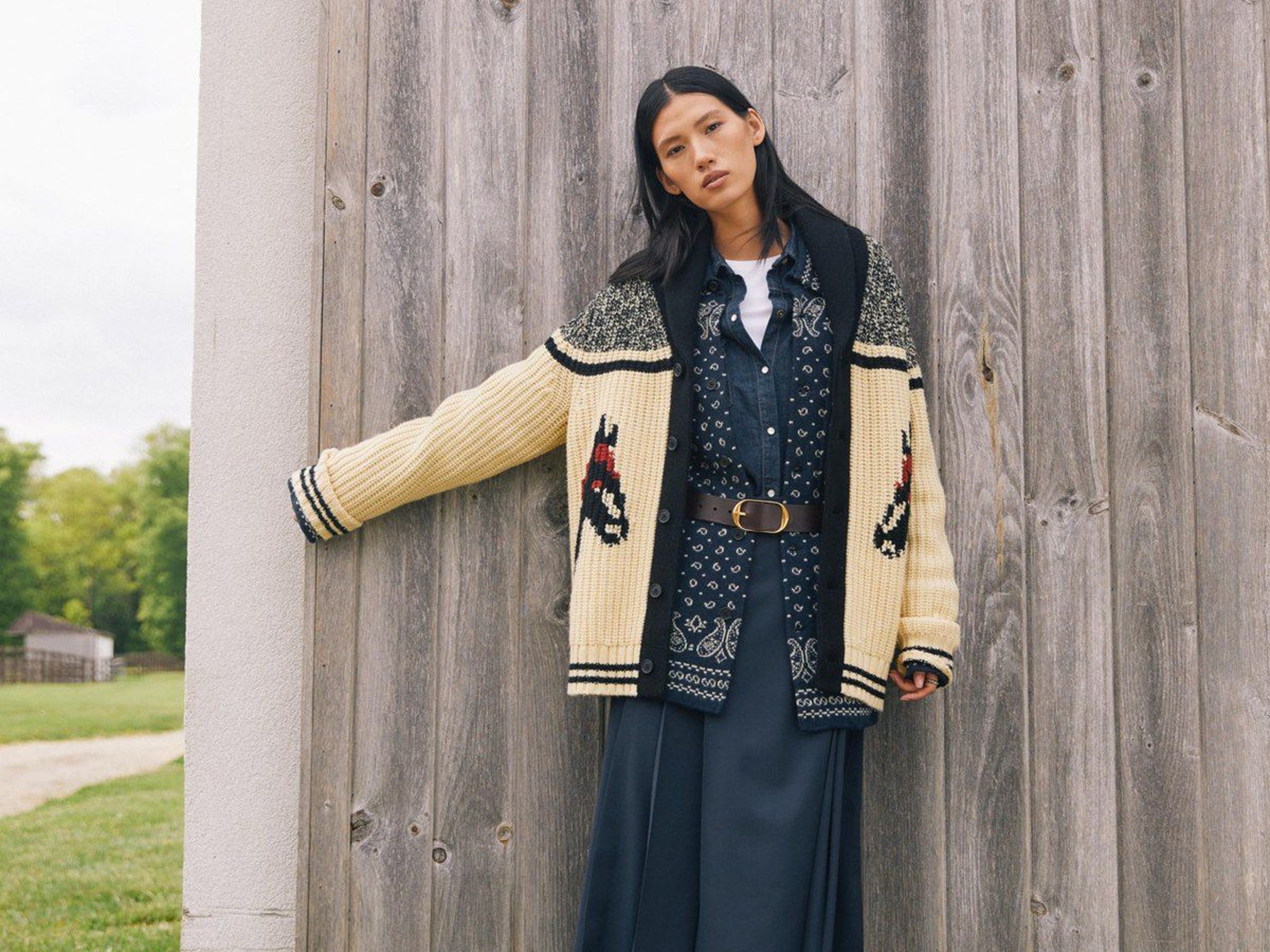 A woman wearing layered boho outfit by wooden wall.