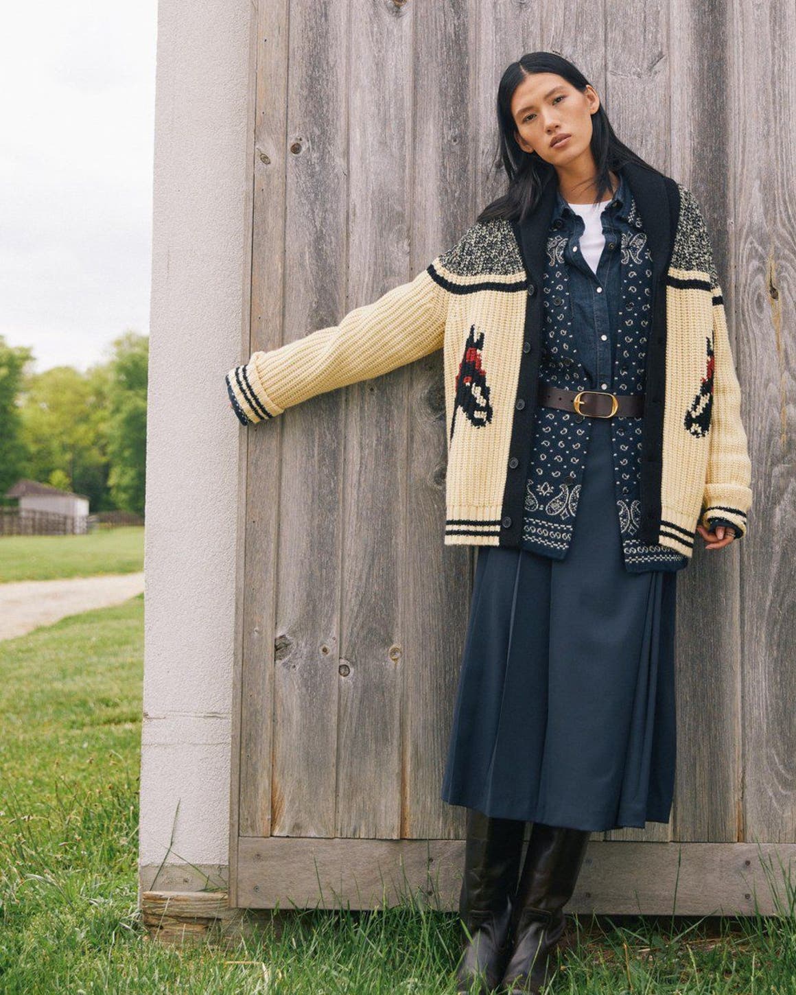A woman wearing layered boho outfit by wooden wall.