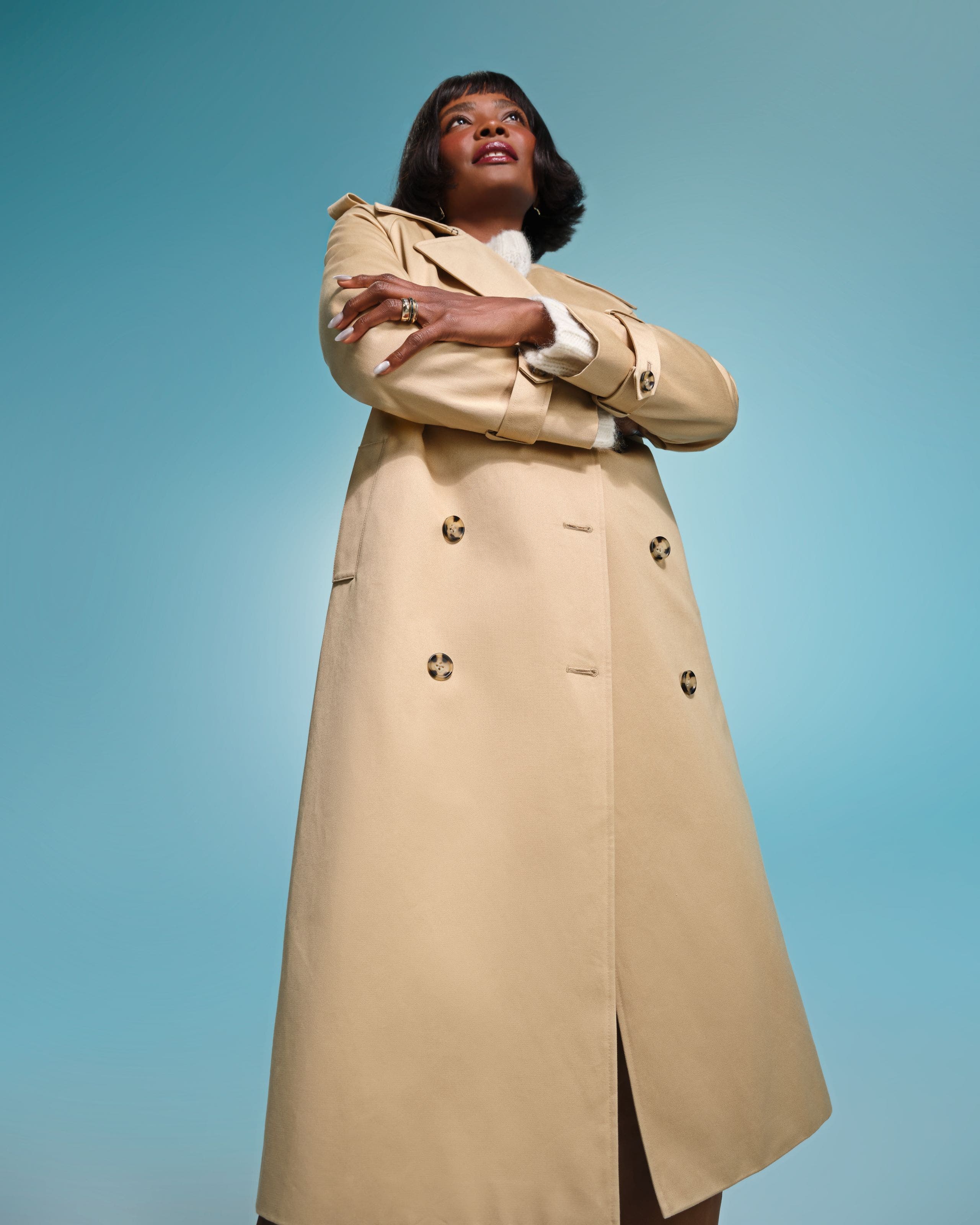 A woman wearing a long khaki trench coat. 