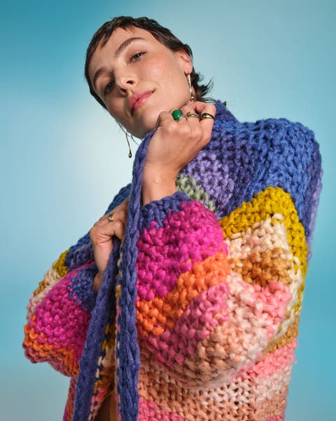 Woman wearing a chunky, multicolored hand-knit sweater with bold stripes.