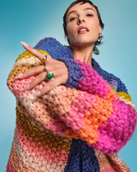 Model wearing an oversized multicolor chunky knit sweater with gold and green statement rings.