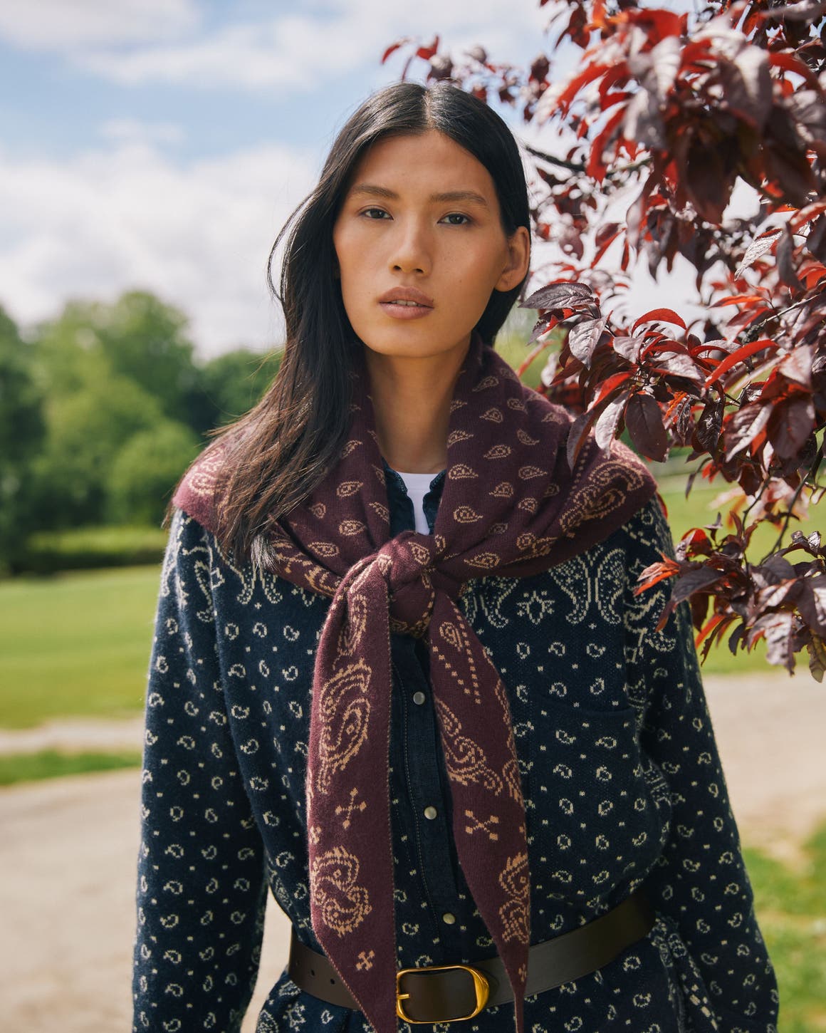 A woman wearing a dark blue patterned shirt and a maroon scarf tied loosely around her neck