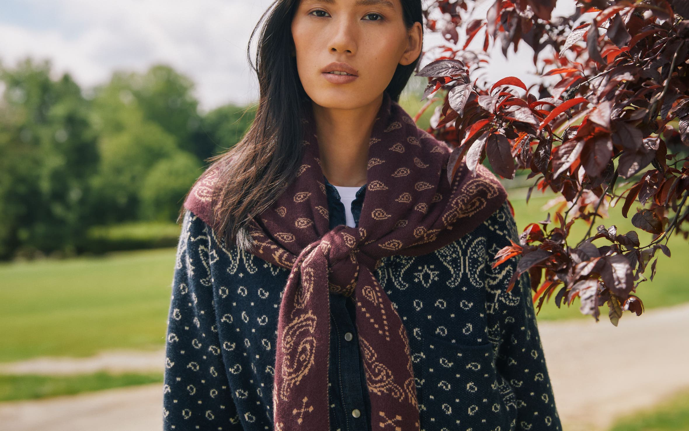 A woman wearing a dark blue patterned shirt and a maroon scarf tied loosely around her neck